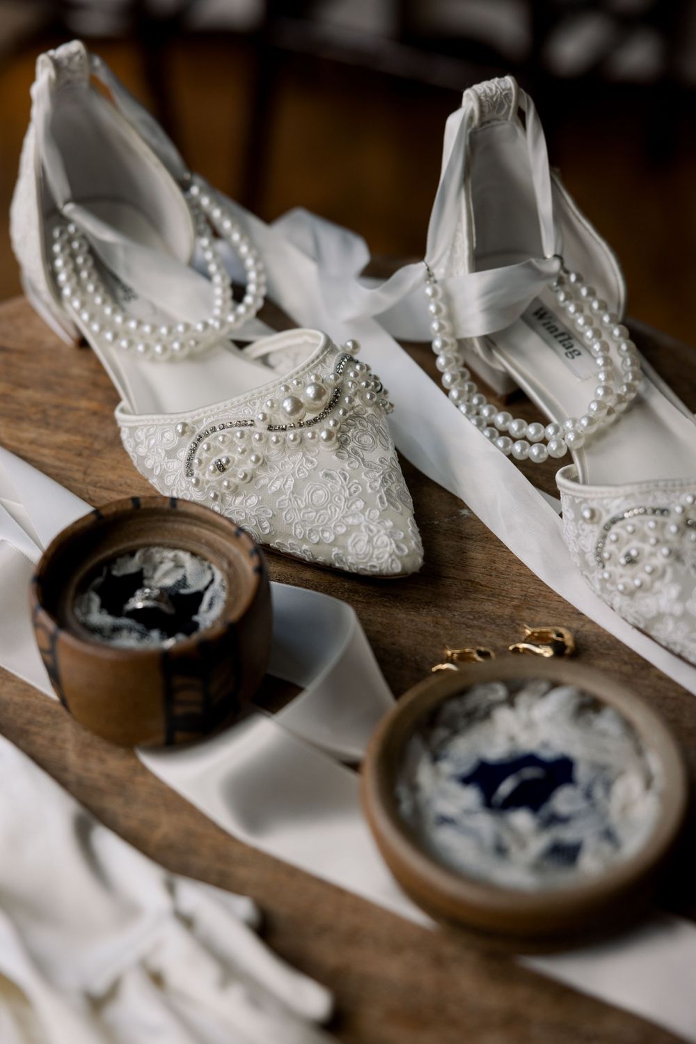 Detailed shot of vintage-style lace wedding flats with pearl straps next to decorative boxes.