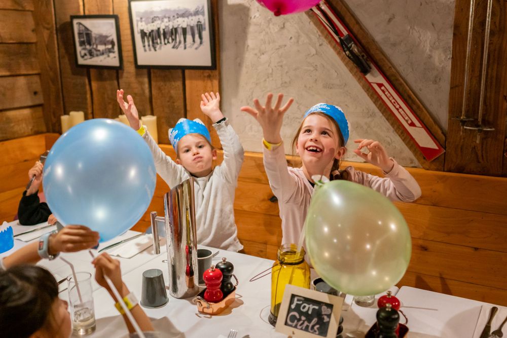 Joyful 7th birthday party photography of a boy blowing out candles with friends in a Snowplanet party room, by an Auckland photographer.