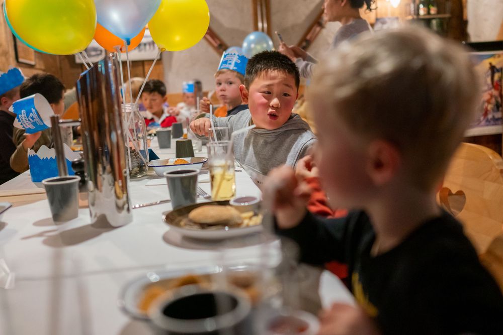 Joyful 7th birthday party photography of a boy blowing out candles with friends in a Snowplanet party room, by an Auckland photographer.