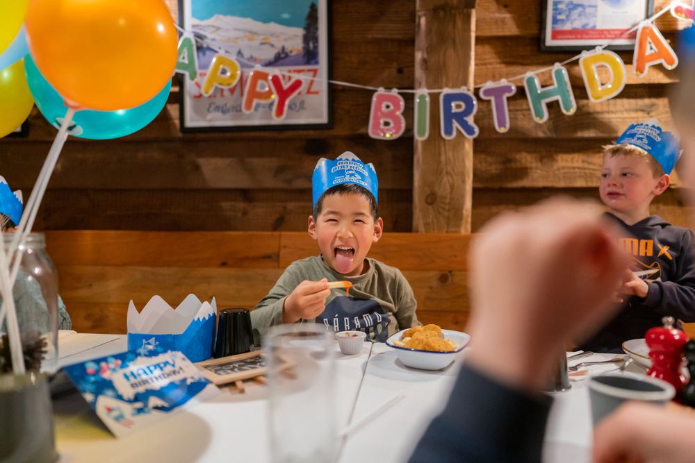 Joyful 7th birthday party photography of a boy blowing out candles with friends in a Snowplanet party room, by an Auckland photographer.