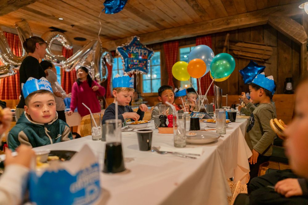 Joyful 7th birthday party photography of a boy blowing out candles with friends in a Snowplanet party room, by an Auckland photographer.