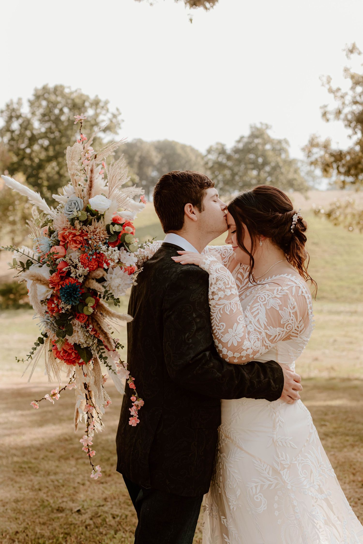 Romantic outdoor wedding photo by a pond with couple in all-white attire sharing an intimate moment.