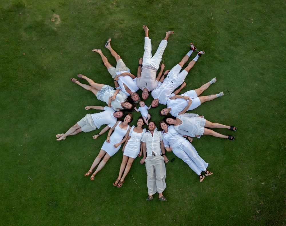 A group of people in white clothes lying in a circular formation on green grass, photographed from above.