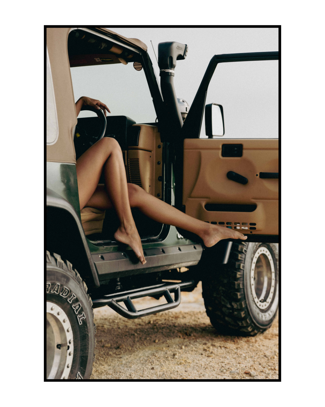 Close-up view of legs hanging out of a Jeep door showing tan interior and rugged tires.