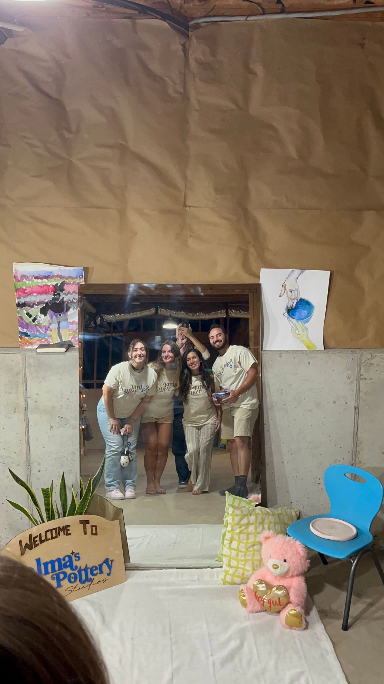 Group of four smiling friends posing in a mirror at Irma's Pottery studio surrounded by colorful artwork.