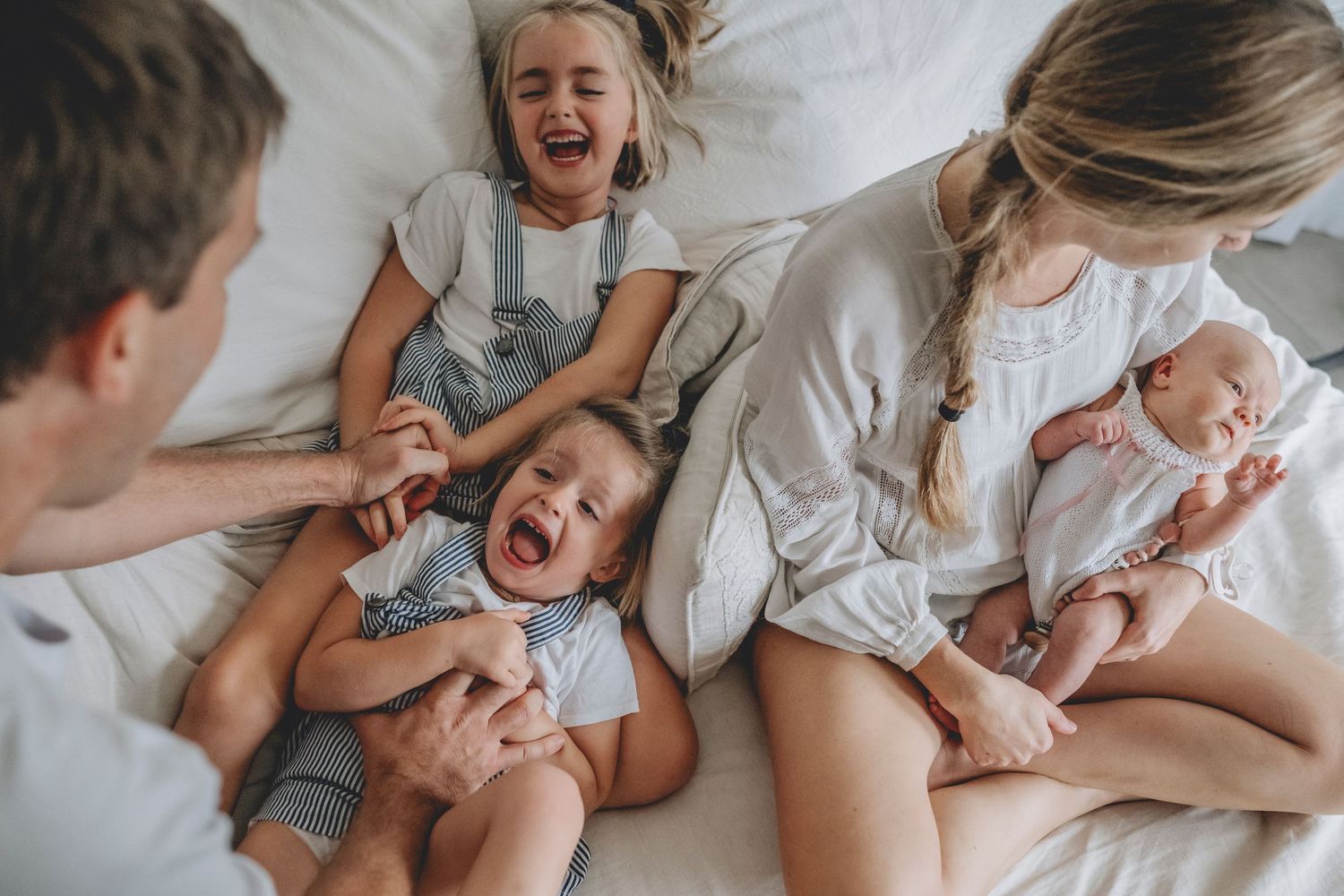niñas de 3 y 6 años en la cama riendo, papa¡á le hace cosiquillas, mamá está sentada con bebé en brazos, en tandil