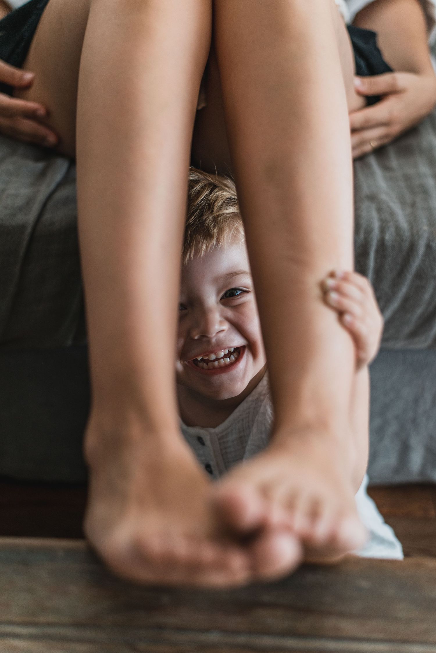 Niño sonriendo escondido entre las piernas de su madre