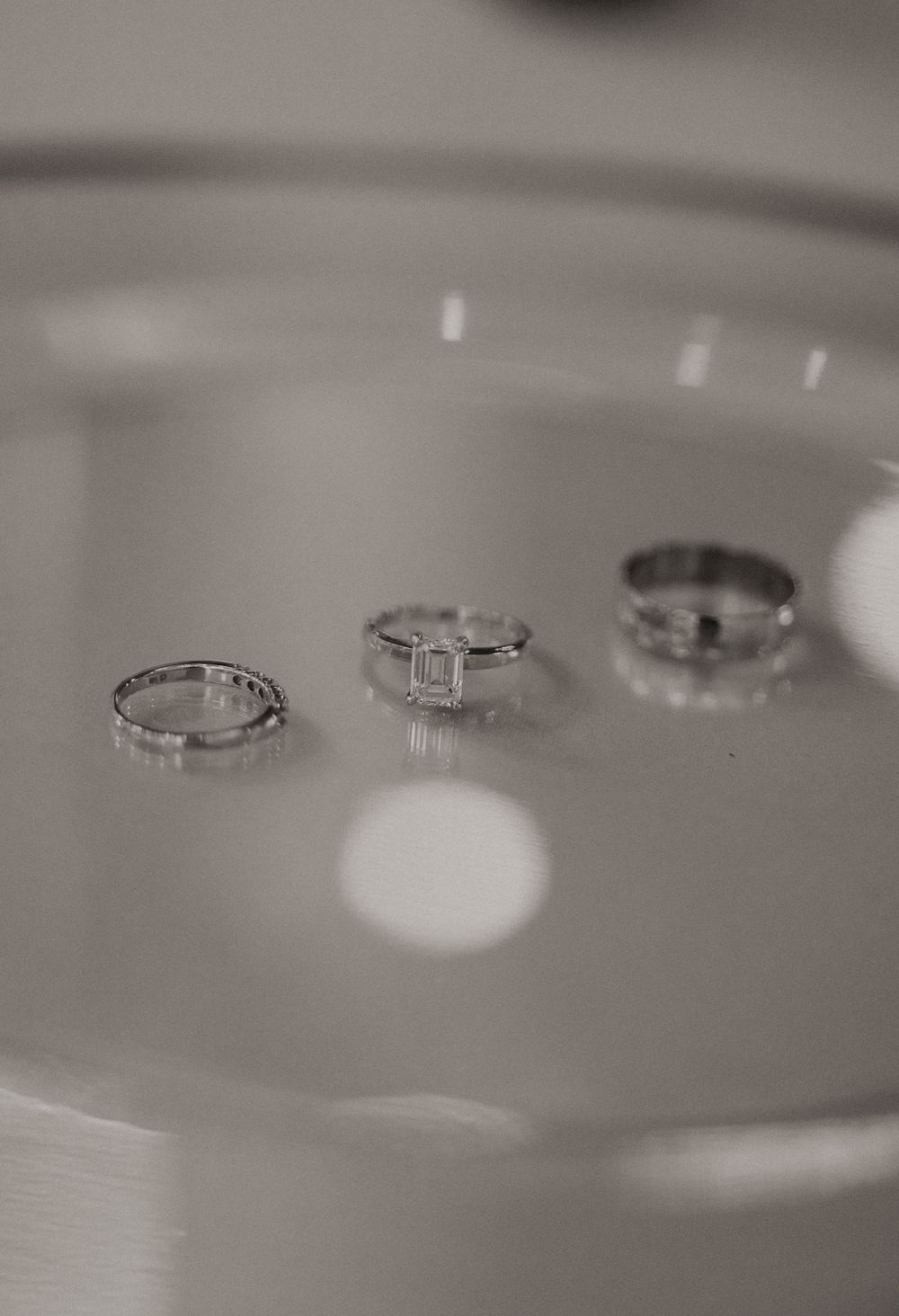 Three elegant wedding rings arranged on a reflective surface in black and white photography.