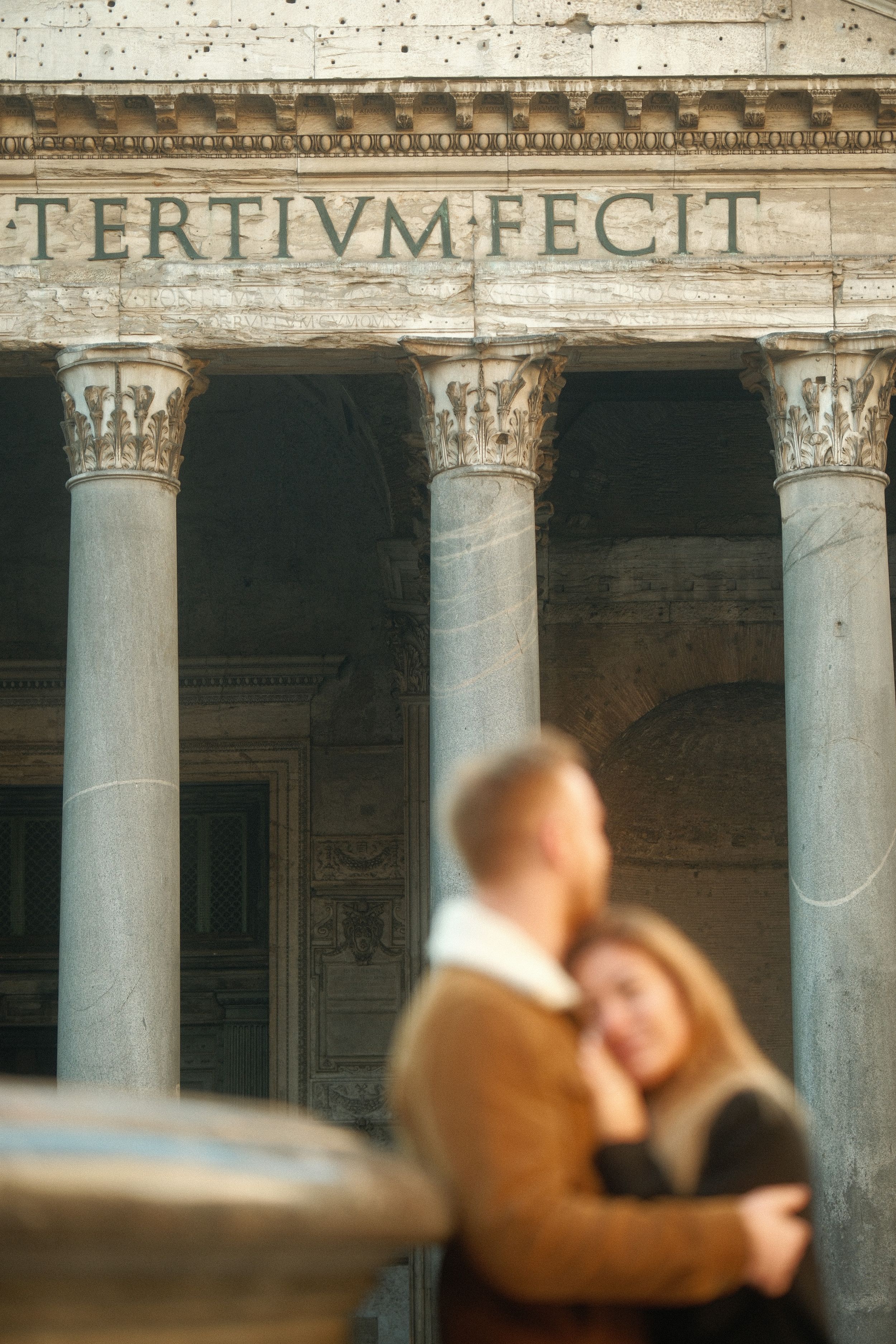 Romantic embrace in front of ancient Roman architecture with the text 'TERTIVM FECIT'.