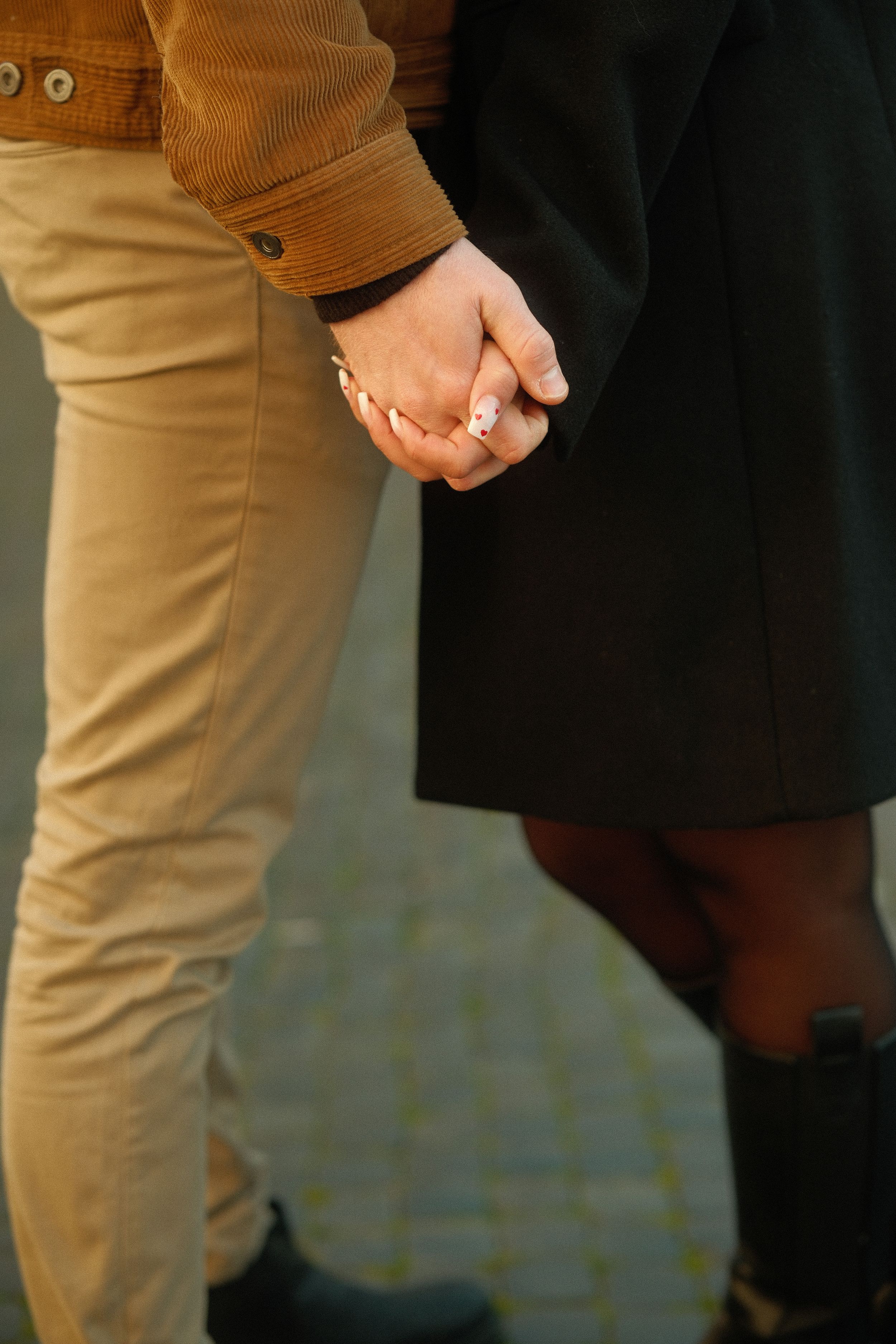 Close-up of two people holding hands, one wearing khaki pants and the other in dark clothing.