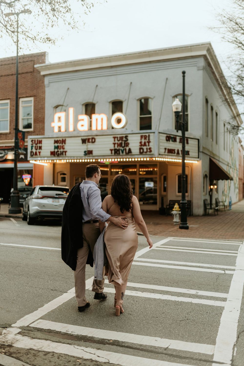 A couple walks arm in arm past the historic Alamo theater with its illuminated marquee.