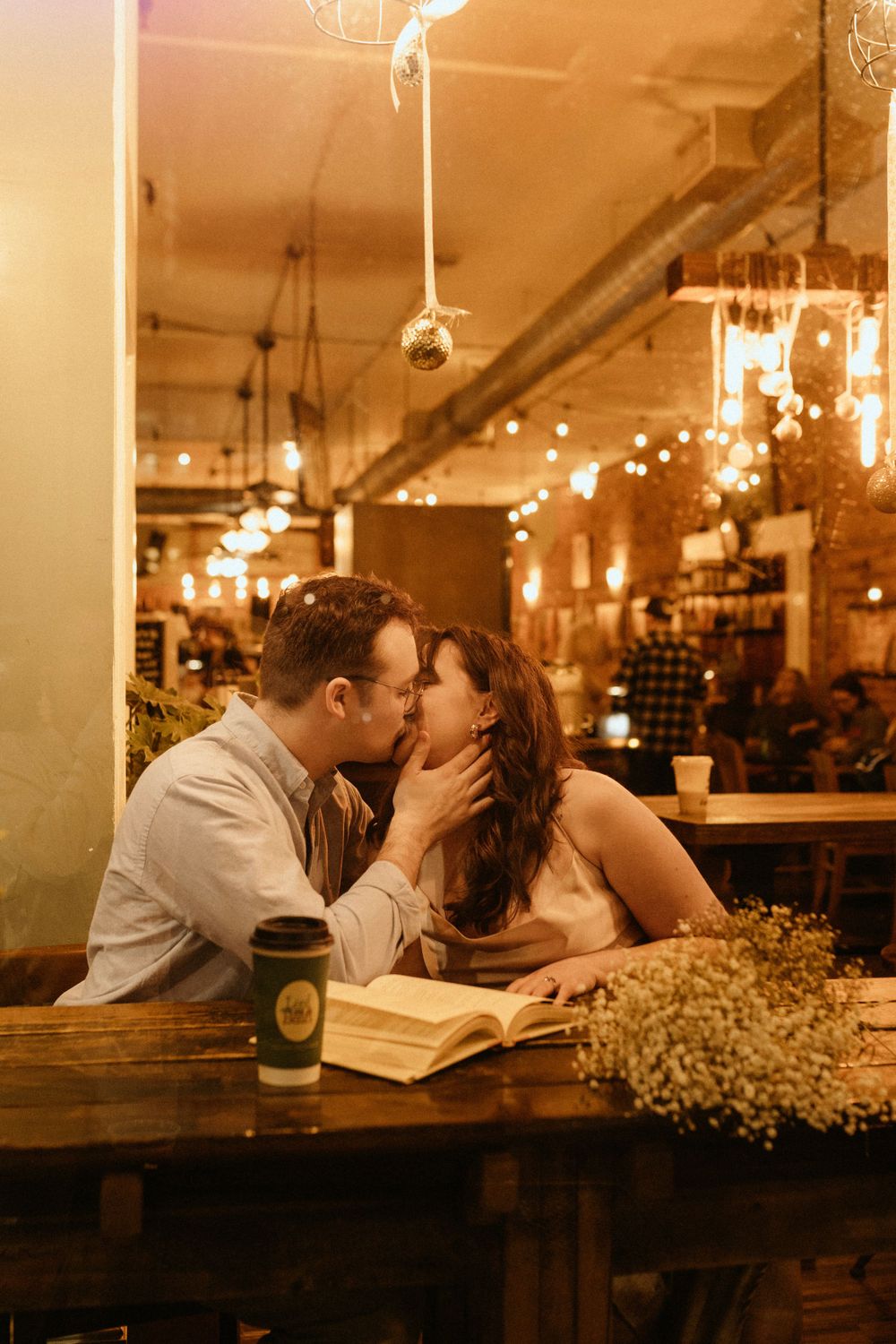 A couple shares a kiss at a rustic restaurant table with warm lighting and baby's breath decor.