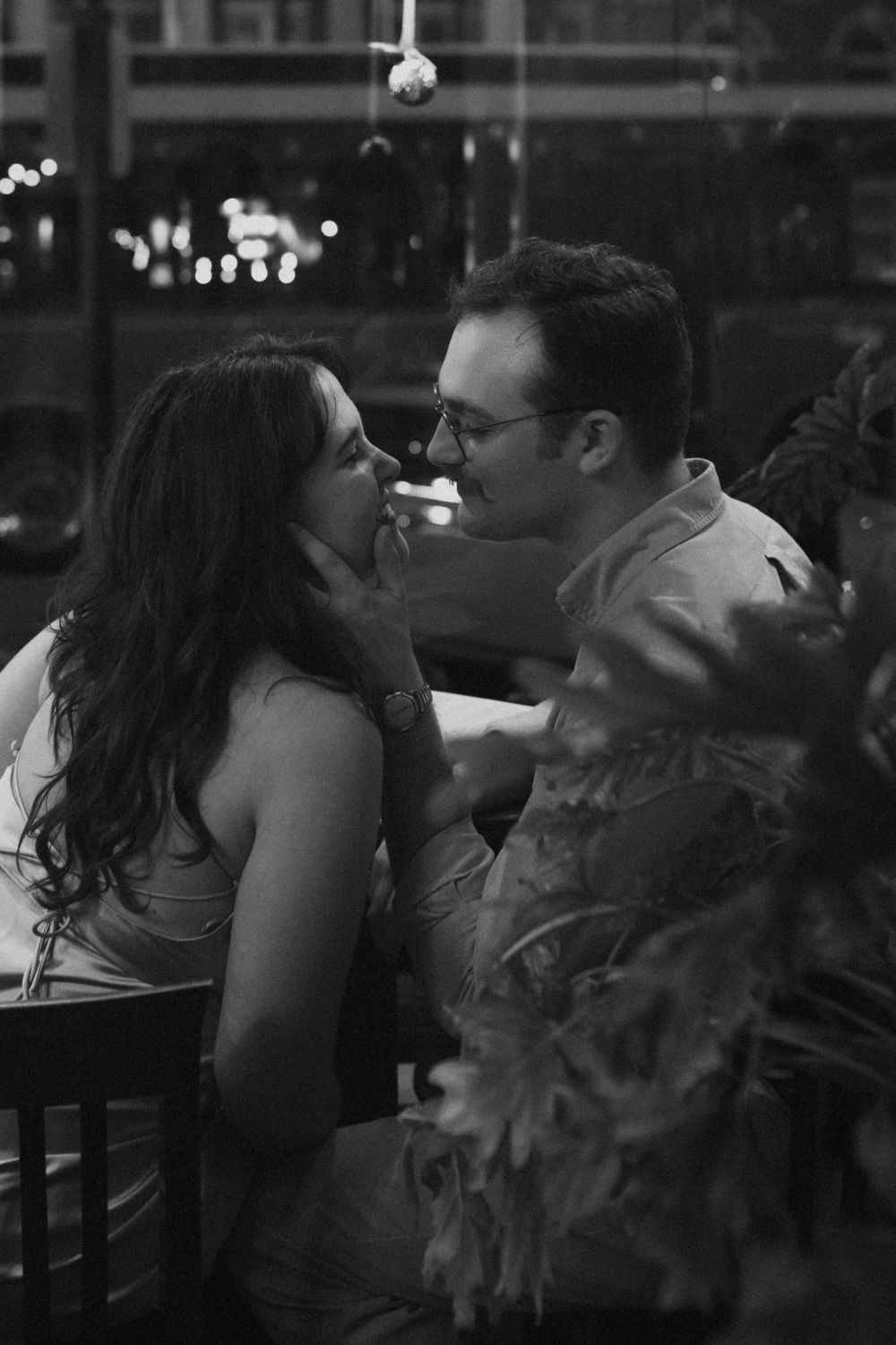 A black and white candid moment between a couple at a dimly lit restaurant table.