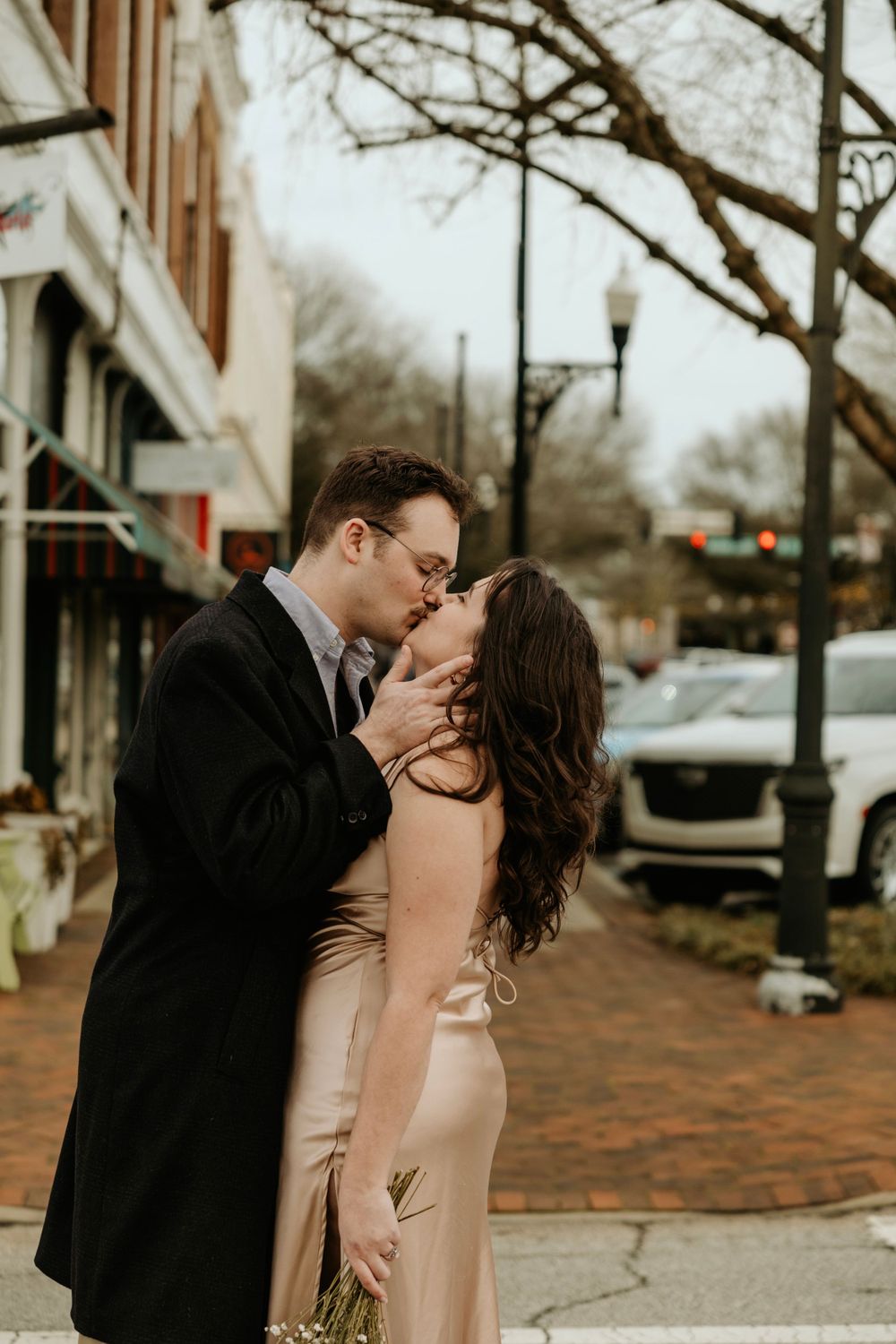 A romantic kiss on a brick sidewalk during an elegant evening photoshoot.