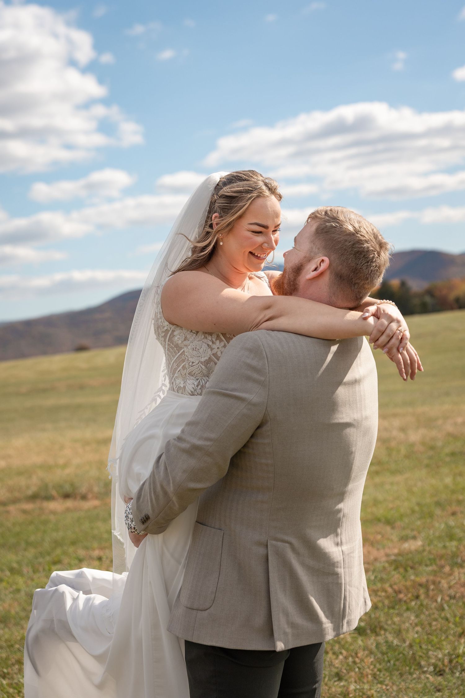 Wedding couple shares a candid laughing moment in front of mountain landscape with coral bouquet.