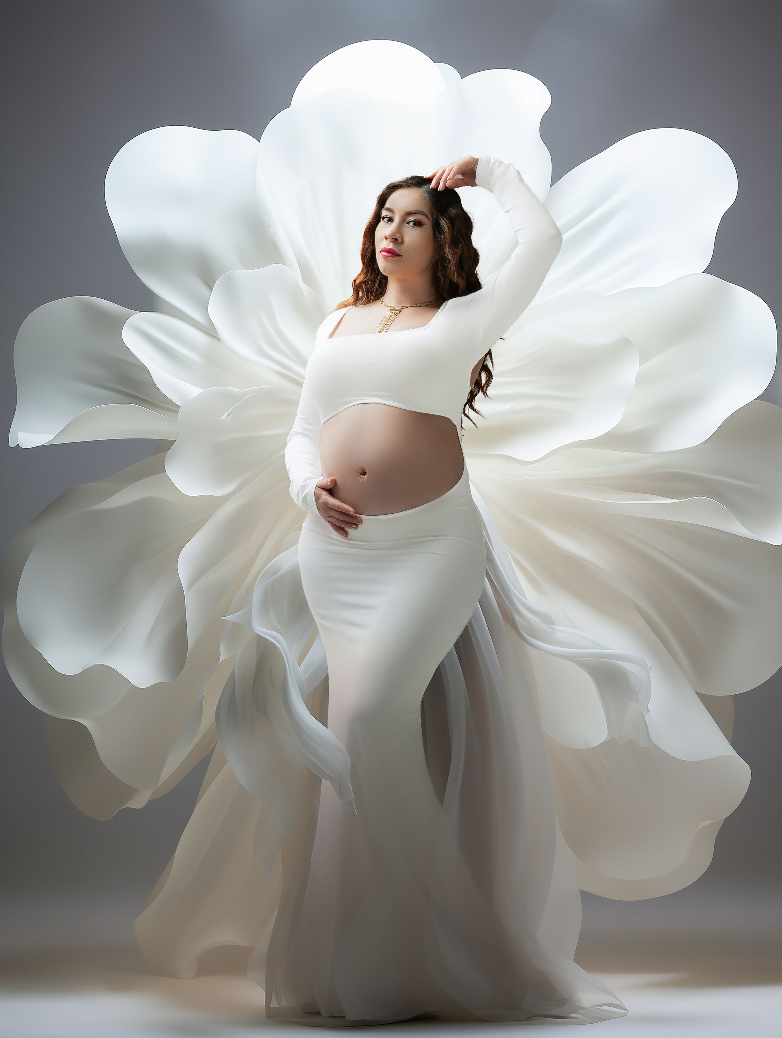 Artistic maternity photo featuring flowing white fabric creating a flower-like effect around the expectant mother.