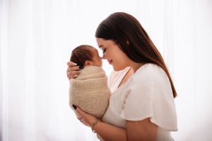 A tender moment between mother and newborn against white backdrop in soft natural light.