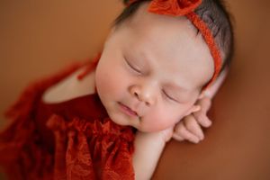 Close-up of sleeping newborn wearing red lace outfit and bow headband.