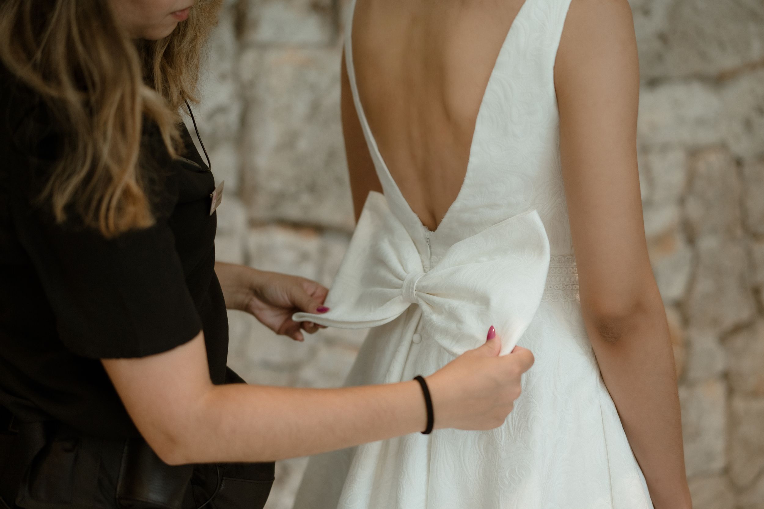Close-up of someone adjusting a white wedding dress bow detail from behind.