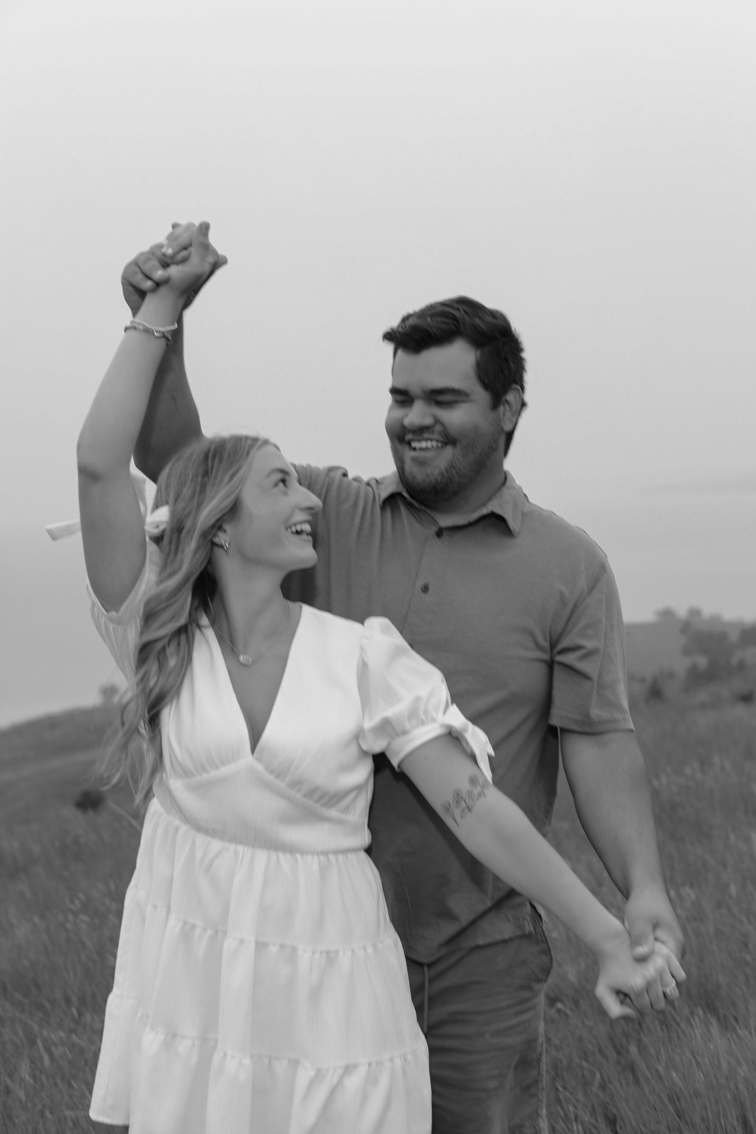 Couple in casual attire dancing and laughing together in a grassy field.