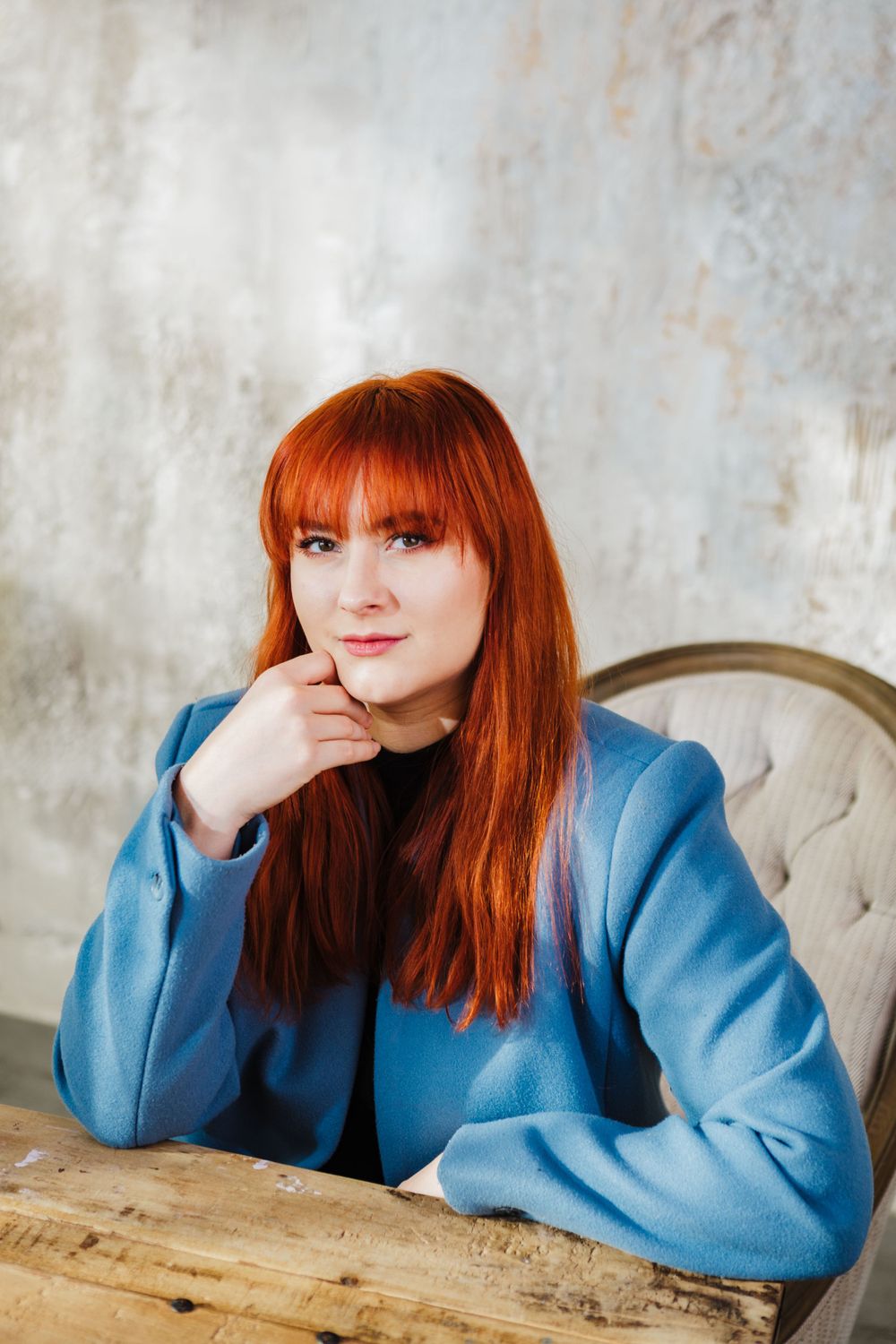 Portrait of a woman in blue sweater sitting at wooden table.