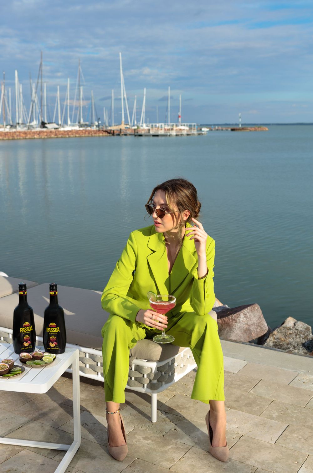 Person in bright yellow suit enjoying drinks by marina with sailboats in background.