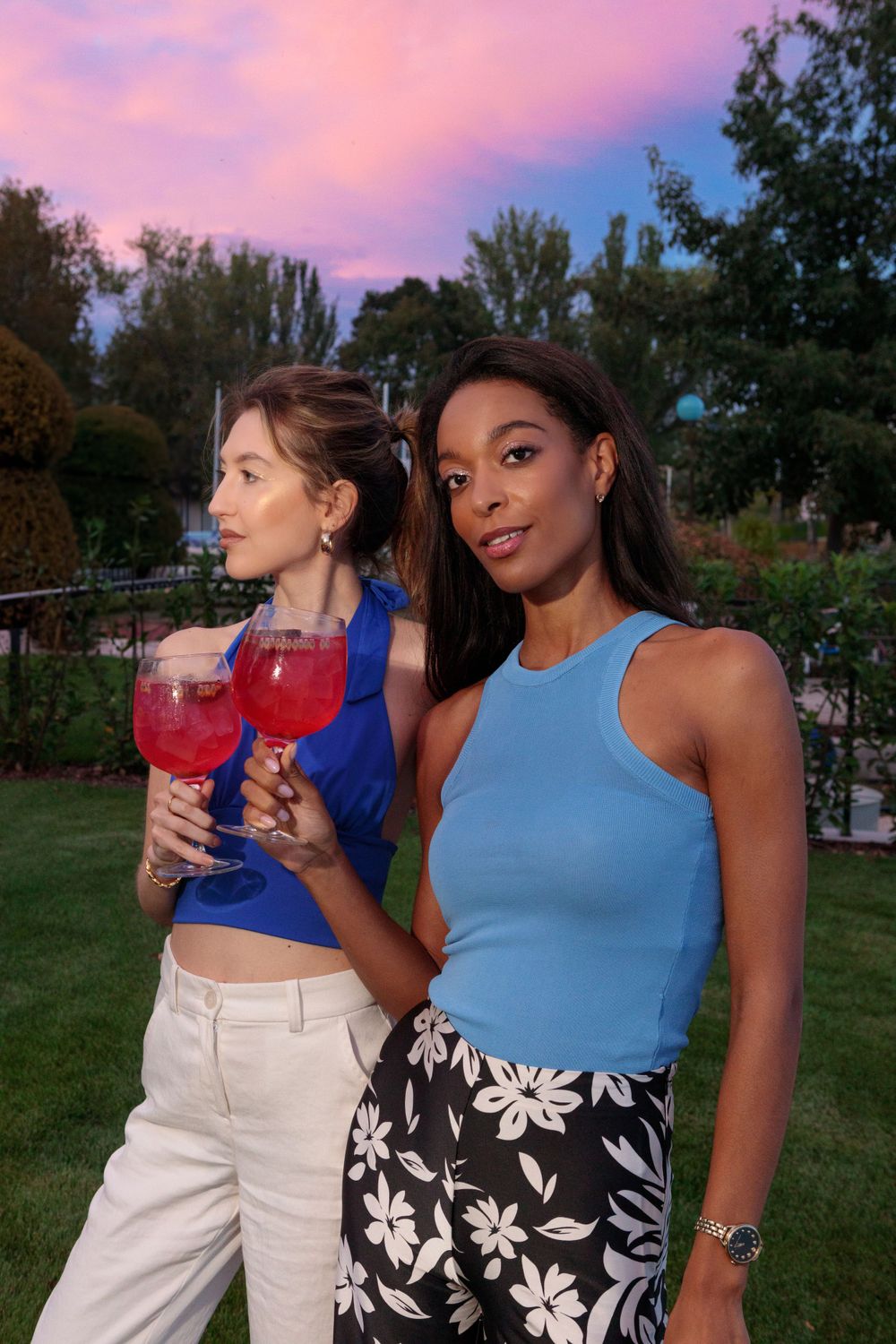Two friends enjoying colorful cocktails at sunset in a garden setting.