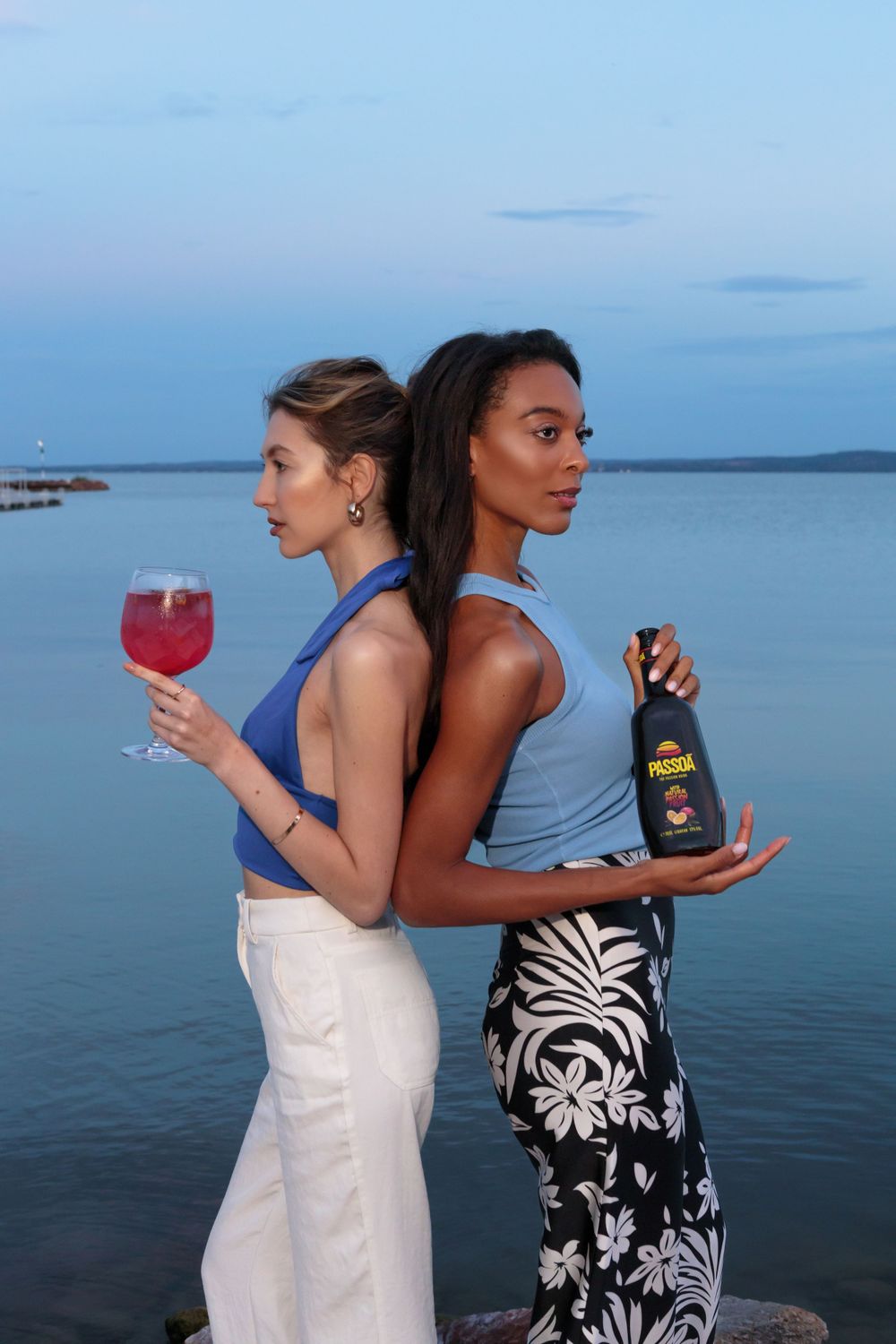 Fashion models posing back to back at sunset with cocktails and wine by the ocean.