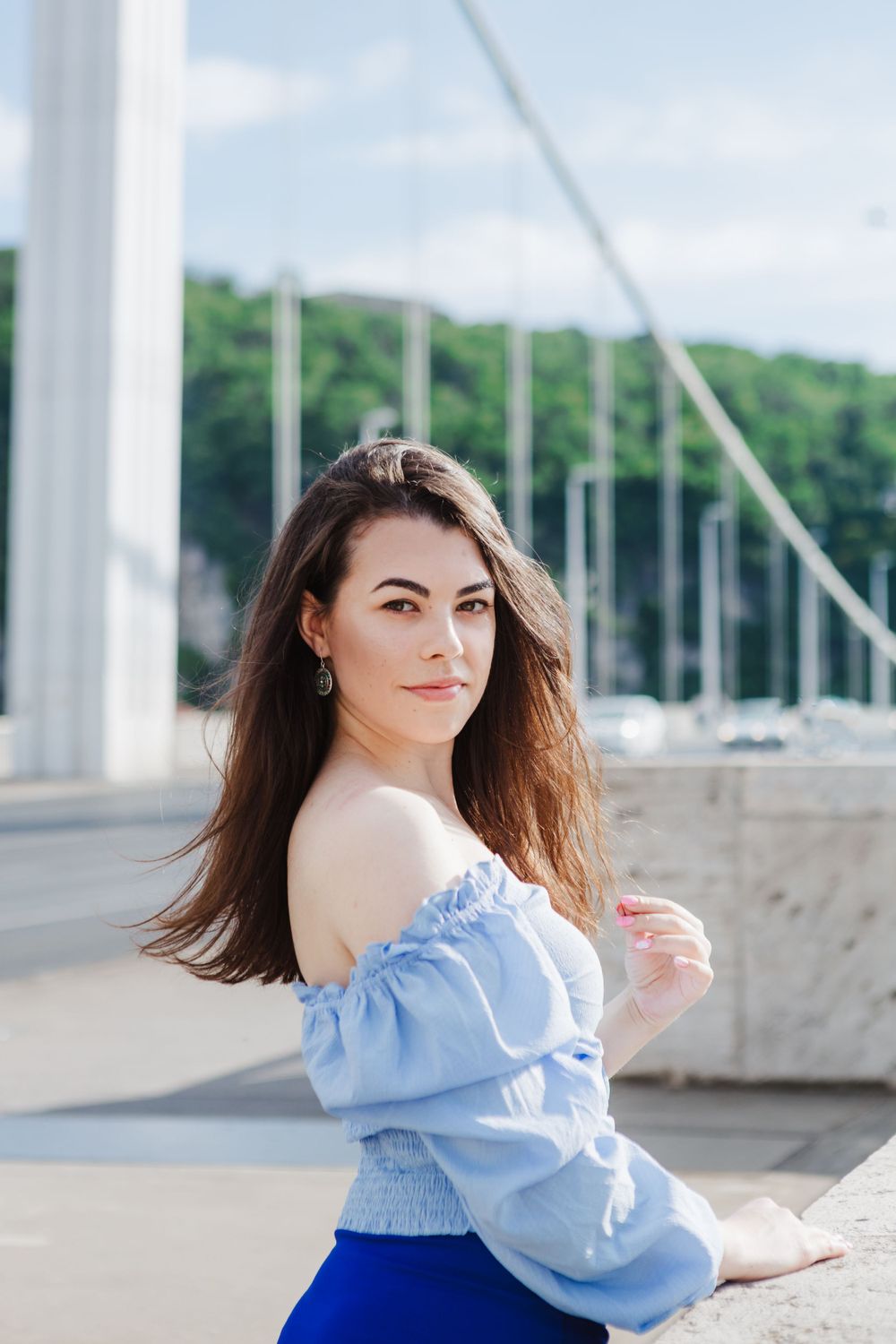 A fashionable look with light blue off-shoulder top and blue skirt at a marina with sailboats in background.