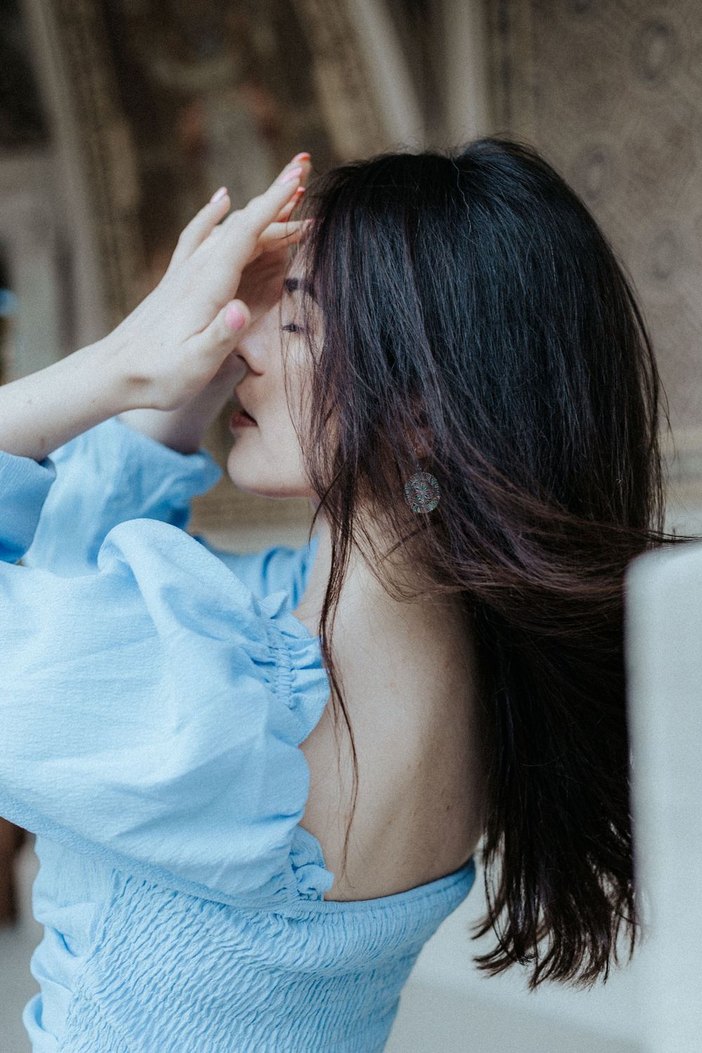 A portrait in soft light featuring a light blue puff-sleeve top and flowing dark hair.