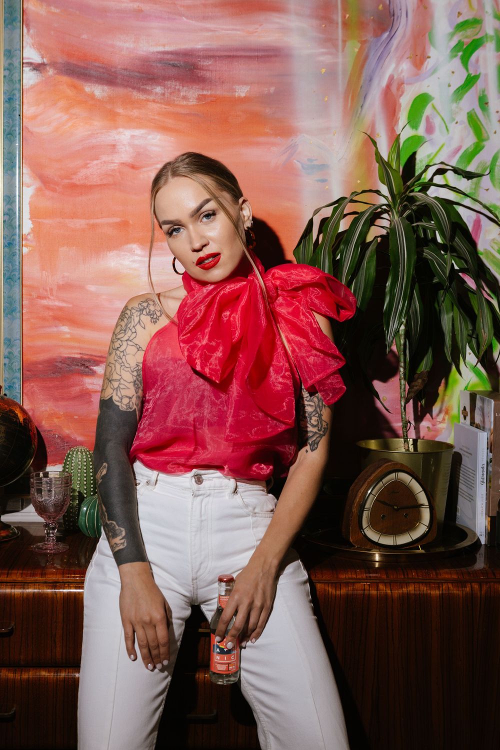 Stylish fashion photoshoot with red ruffled blouse, white pants and tropical plants against coral colored backdrop.