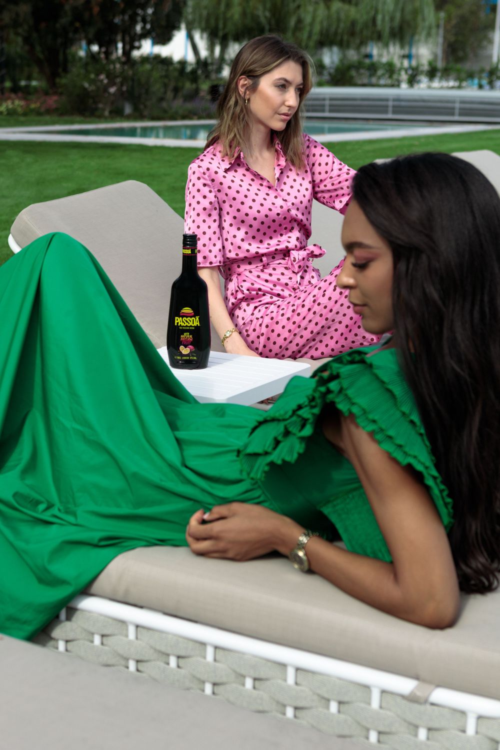 Friends relaxing on outdoor lounge chairs in pink polka dot and emerald green dresses.