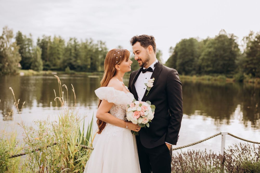 A romantic lakeside portrait of newlyweds holding a pink and white bouquet.
