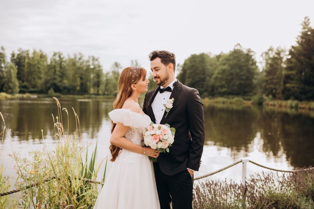 A tender wedding moment captured by a serene lake with trees in the background.