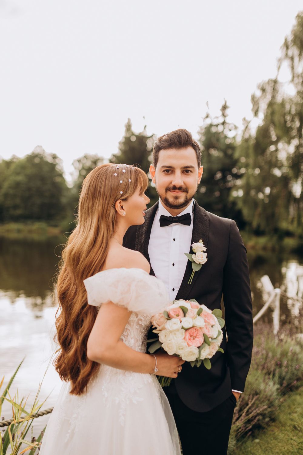 An intimate wedding portrait by a lake with the bride holding a pink and white bouquet.