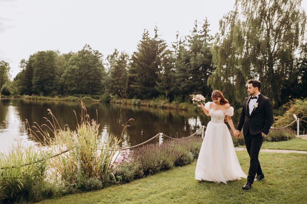 A joyful wedding couple walking along a lakeside path surrounded by nature.