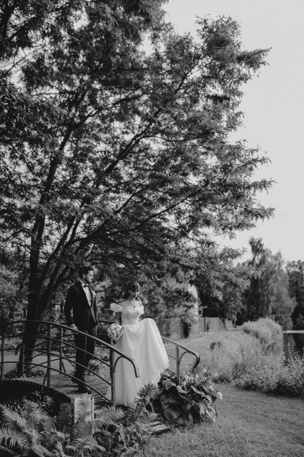 A romantic bridge photo with a couple posing beneath overhanging tree branches in monochrome.