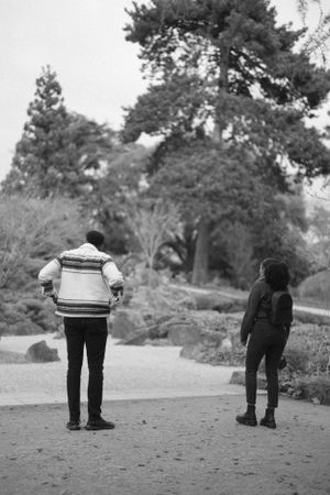 Two people standing apart on a garden path in black and white photography.