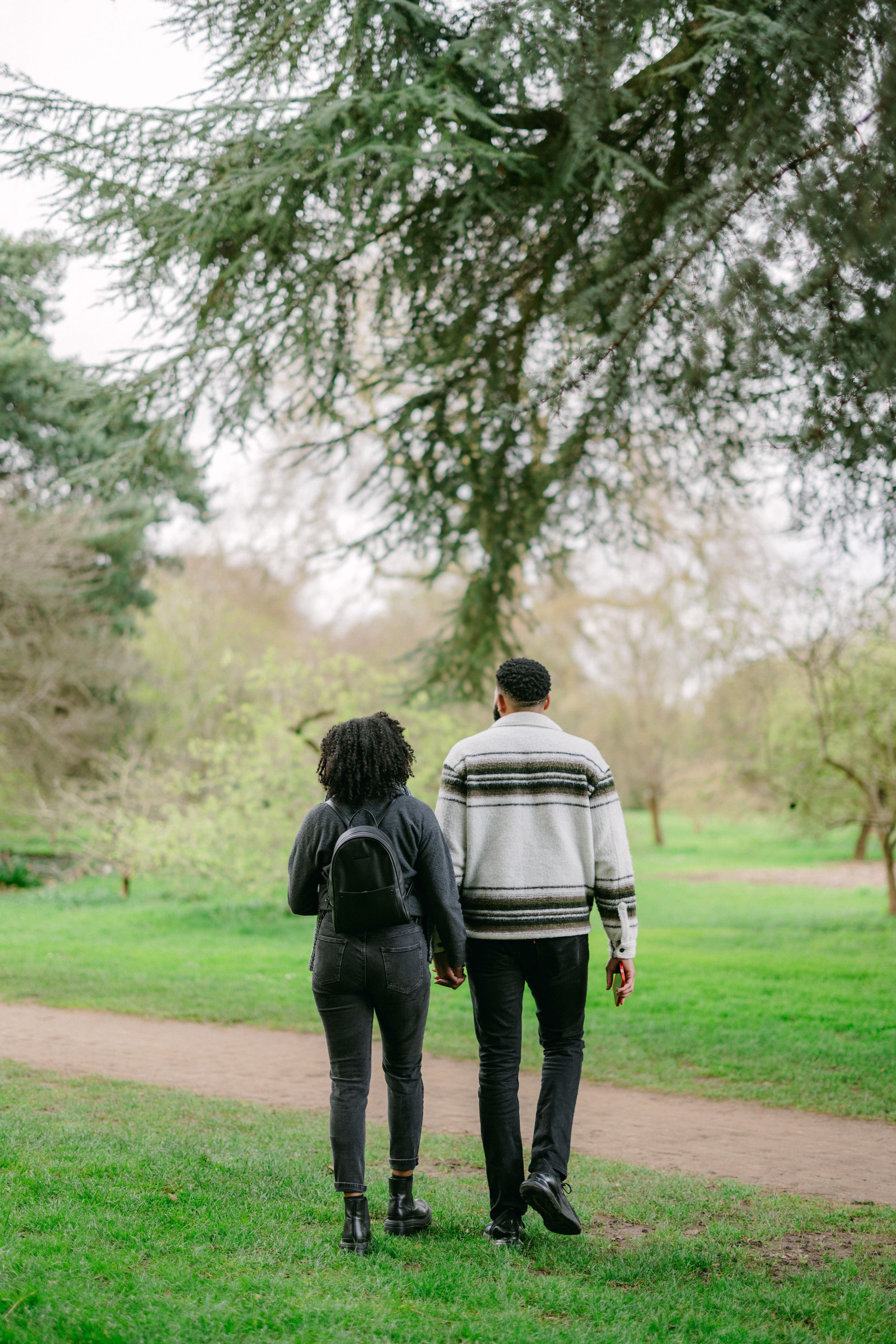 A couple strolling together on a dirt path under overhanging trees.