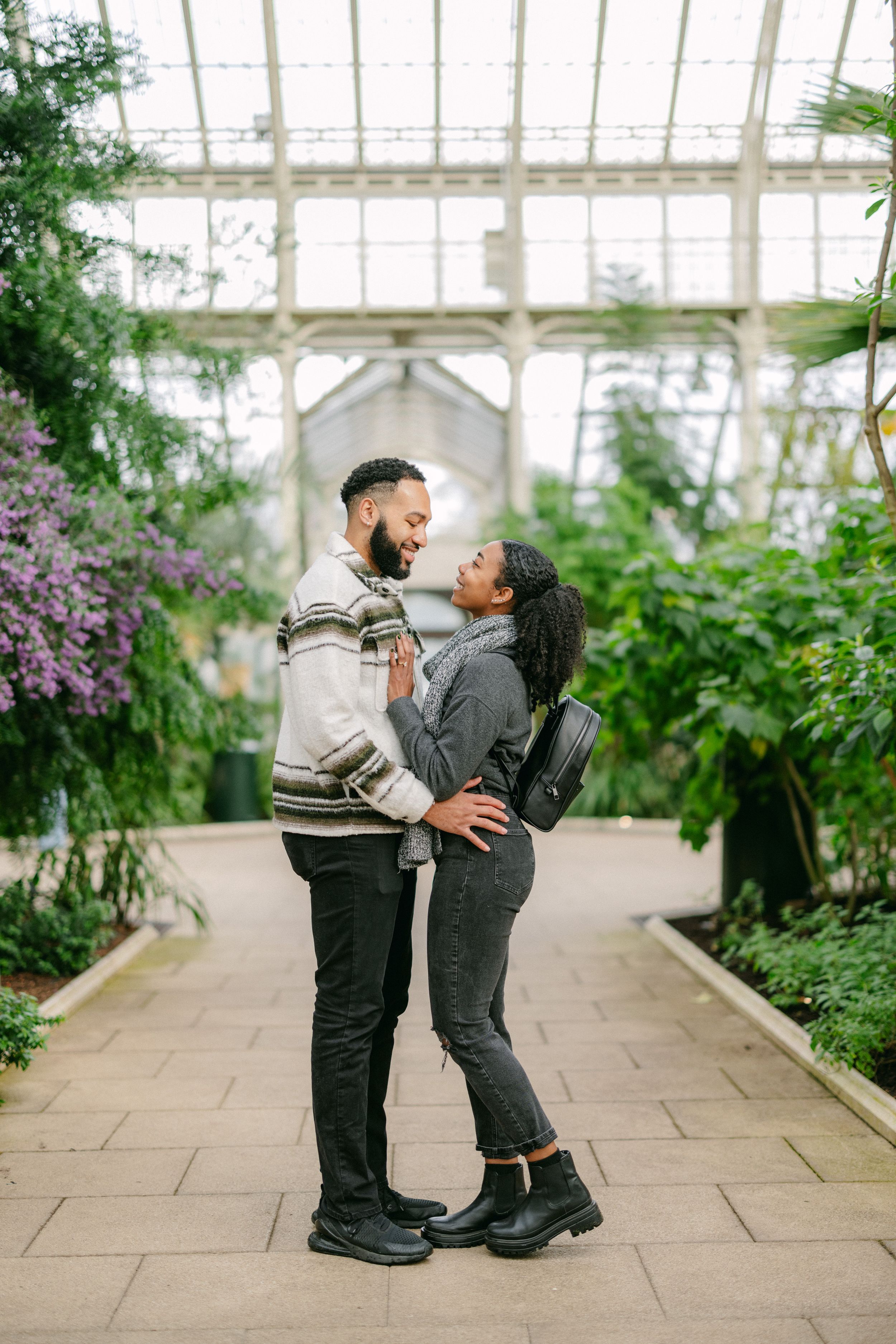 A couple sharing an intimate moment in a sunlit greenhouse filled with plants.