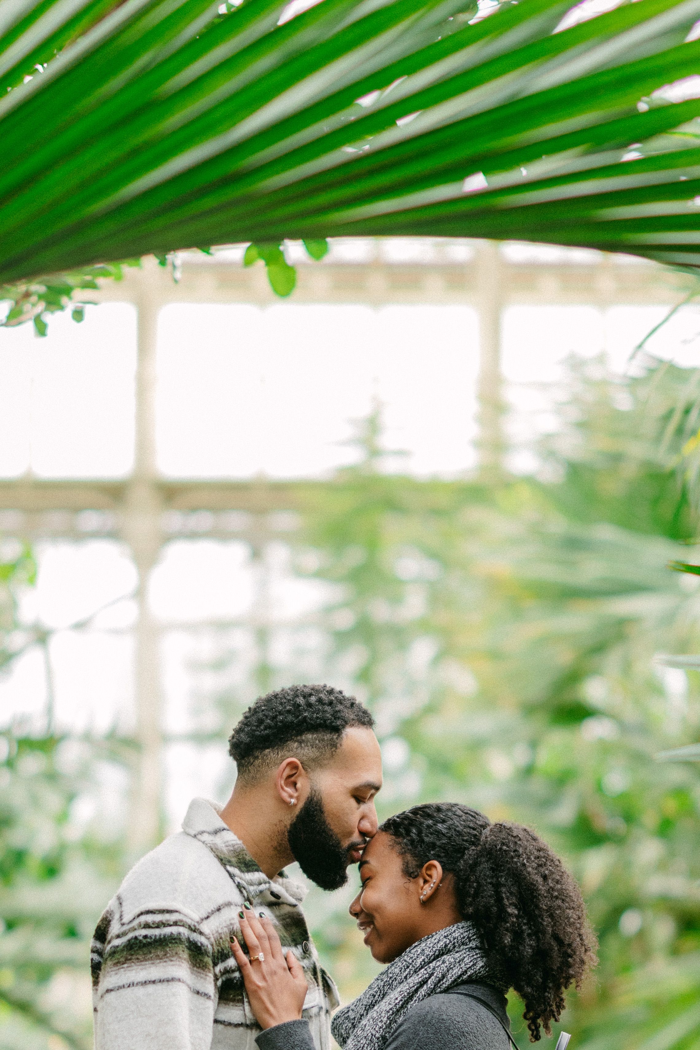 A tender moment shared between a couple under tropical foliage in a greenhouse.