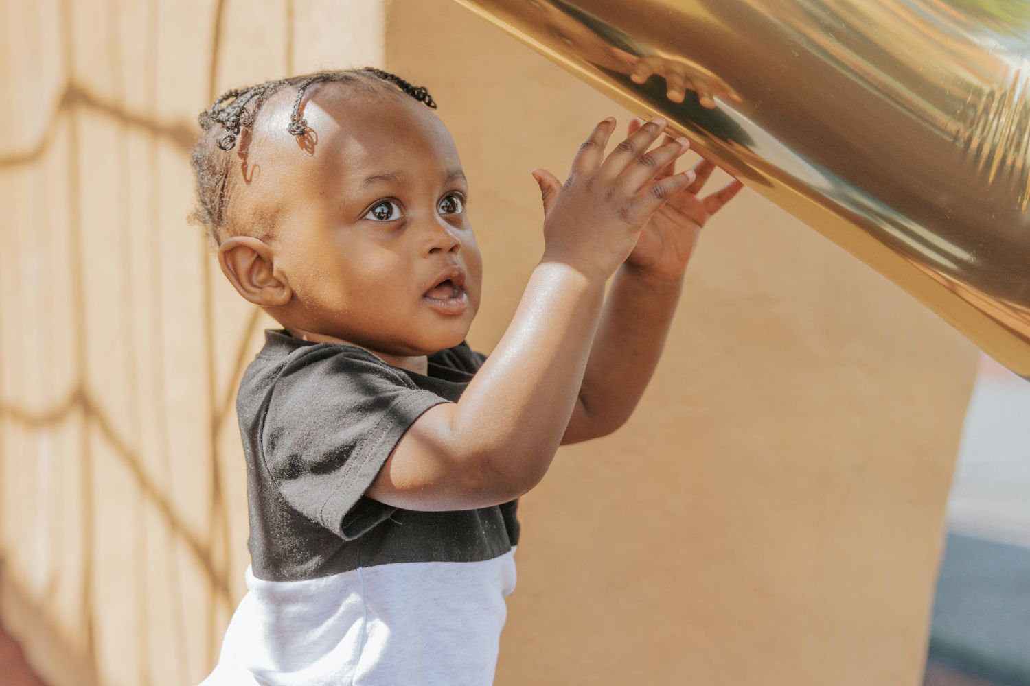 A small child reaches up towards a shelf while wearing a gray shirt and white garment.
