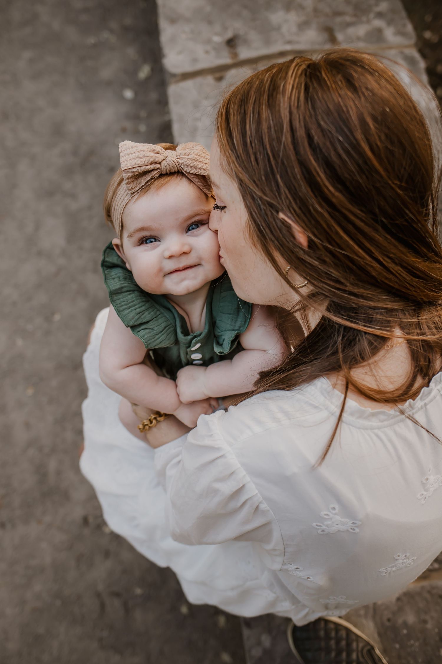Photography of mother kissing her babies cheek as baby smiles at the camera. Photographer captured over head shot in St. Charles County.