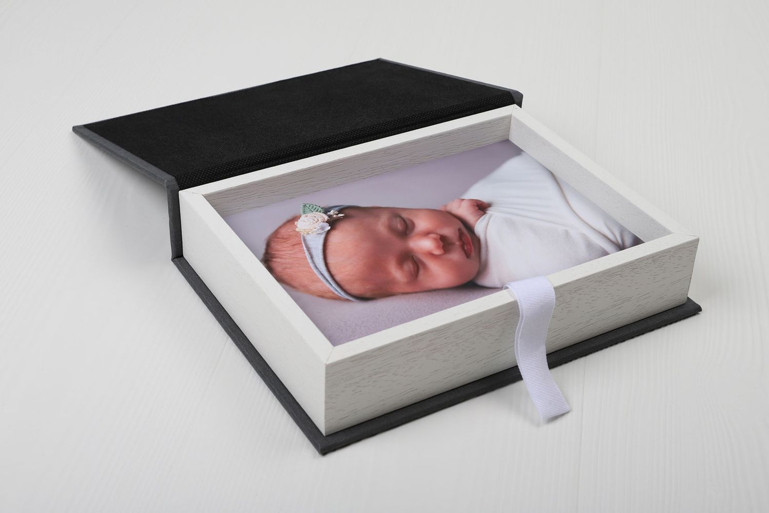 Une boîte photo professionnelle contenant un portrait de nouveau-né avec un ruban blanc à tirer.