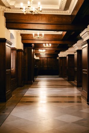 Elegant hallway with wooden paneling and ornate ceiling featuring crystal chandeliers.