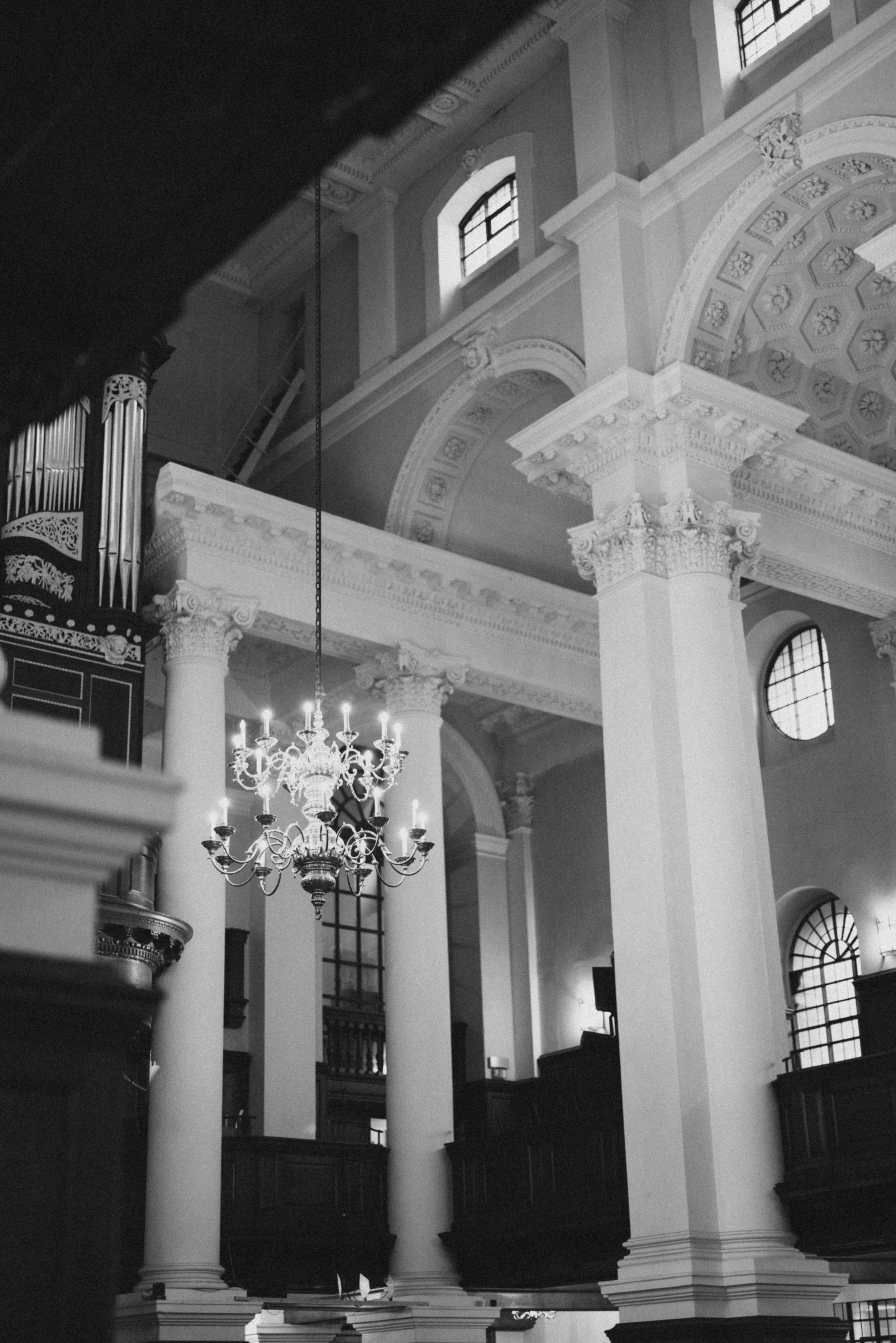 Interior view of a grand church with ornate columns, arches and a chandelier in black and white.