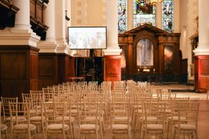 Rows of empty chairs set up in a historic church venue with wood paneling and columns.