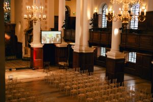 Elegant church interior with rows of chairs and chandeliers leading to a podium with display screens.