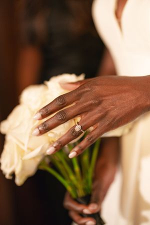A close-up of hands holding white roses with an engagement ring sparkling in the light.