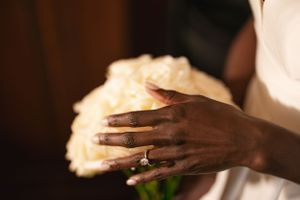 Close-up of hands holding a white rose bouquet with wedding ring visible.